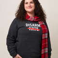 Smiling woman wearing a gray, heathered crewneck sweatshirt with the text DISARM HATE printed in white with a red line through the word HATE.