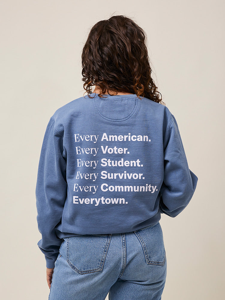 Back view of woman wearing a light blue crewneck sweatshirt with large white print that reads: Every American. Every Voter. Every Student. Every Survivor. Every Community. Everytown.