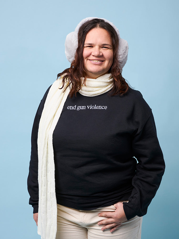 Front view of person wearing a black crewneck sweatshirt with the phrase end gun violence embroidered in white, all lowercase, in a serif font.