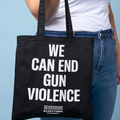Woman holding black canvas tote bag with bold, white all caps text that reads WE CAN END GUN VIOLENCE. Small white Everytown for Gun Safety logo centered beneath text.