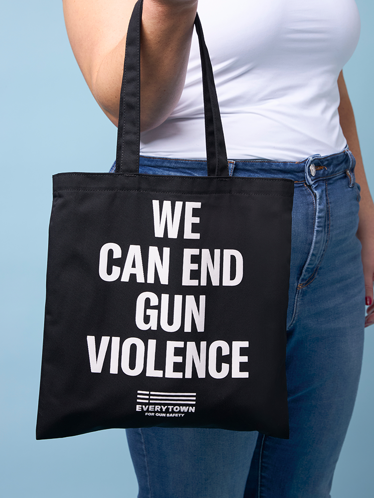 Woman holding black canvas tote bag with bold, white all caps text that reads WE CAN END GUN VIOLENCE. Small white Everytown for Gun Safety logo centered beneath text.