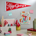 Red felt pennant with white cursive text  that reads Keep Going with a white heart to the right of the text