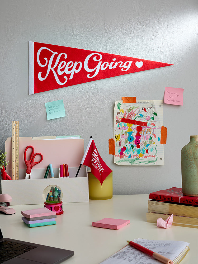 Red felt pennant with white cursive text  that reads Keep Going with a white heart to the right of the text