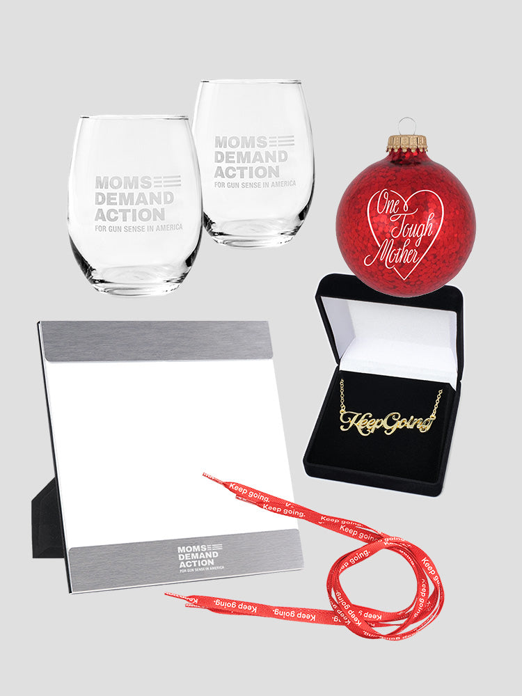 Set of 2 etched wine glasses with Moms Demand Action logo, silver 5x7 inch picture frame with white Moms Demand Action logo, red, sparkly round ornament with white text that reads One Tough Mother in script font with a white heart around it, a gold nameplate-style necklace that reads Keep Going in script font, and red shoelaces with white text that read Keep Going.