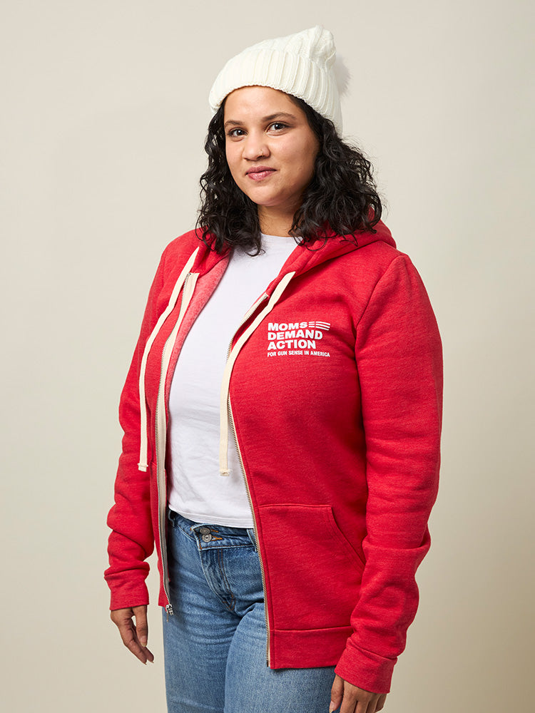 Front view of woman wearing a red zip-up hooded sweatshirt with two front pockets and a small white Moms Demand Action logo printed on left chest.