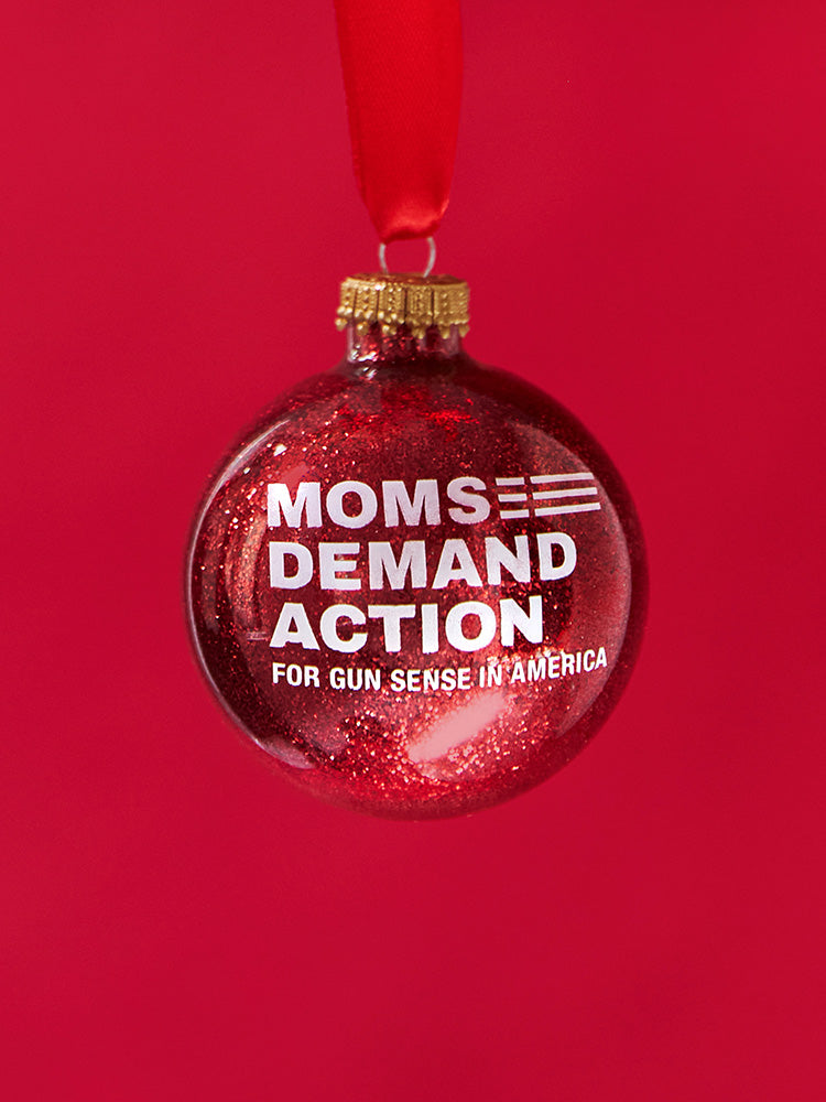 Red, glittery, round plastic ornament with white Moms Demand Action logo printed on one side.