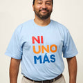 Front view of a man wearing a light blue short sleeve unisex t-shirt with print that reads NI UNO MÁS in large, uppercase, red, orange, and blue letters.