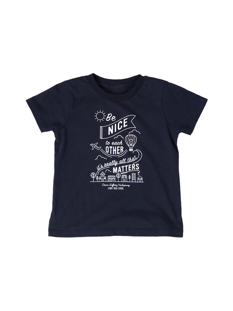 A navy blue short sleeve kids tee shirt. Illustrations of a sun, clouds, hot air balloon, airplane, trees, and buildings surround the quote "Be nice to each other. It's really all that matters." In small letters at the bottom, the quote is credited to "Dawn Lafferty Hochsprung, Sandy Hook School"